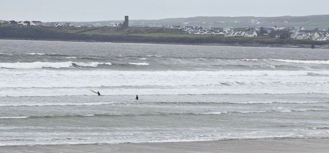 solid swell on the beach as a couple of surfers are walking to get past the whitewater